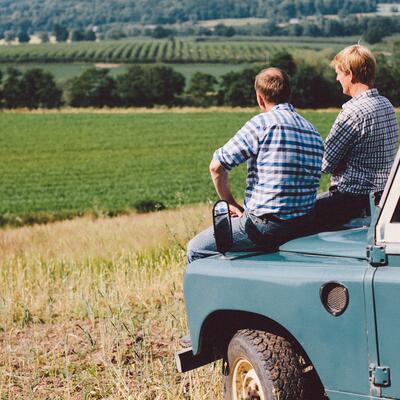 Two men sat on landrover overlooking fields